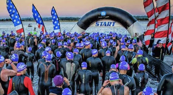 Triathletes massed at the swim start under a SetUp Events arch